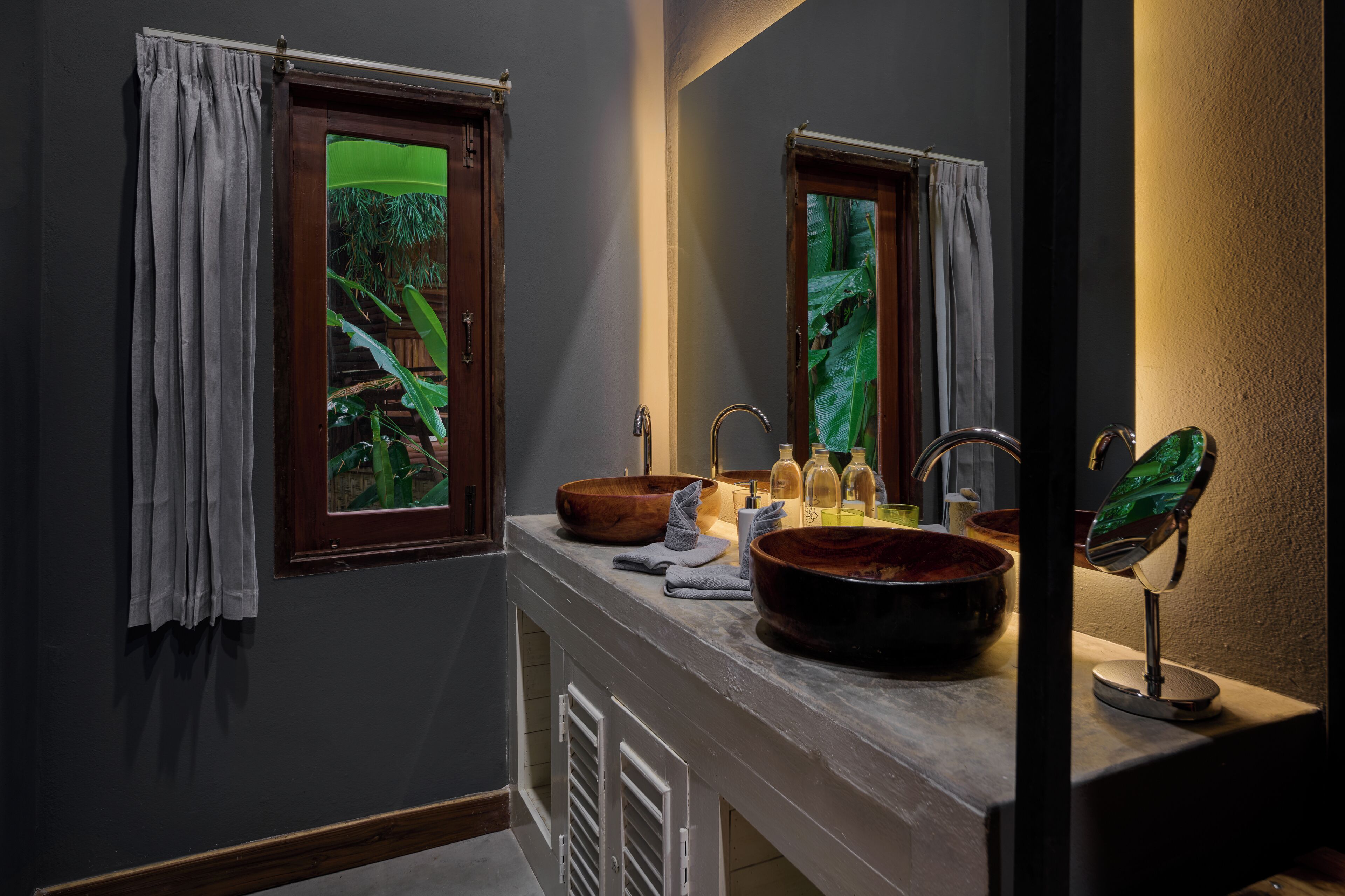 Un bagno con un lavabo in legno, due specchi e una finestra che si affaccia sul verde.