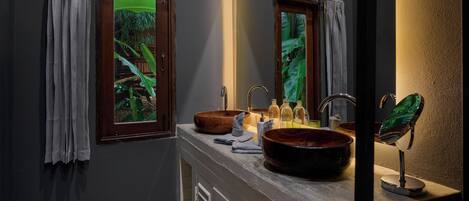 A bathroom with a large wooden bowl sink, two mirrors, and a window with a view of greenery.