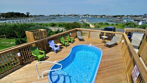 Une terrasse en bois avec une piscine, des chaises longues et une vue sur le port de plaisance.
