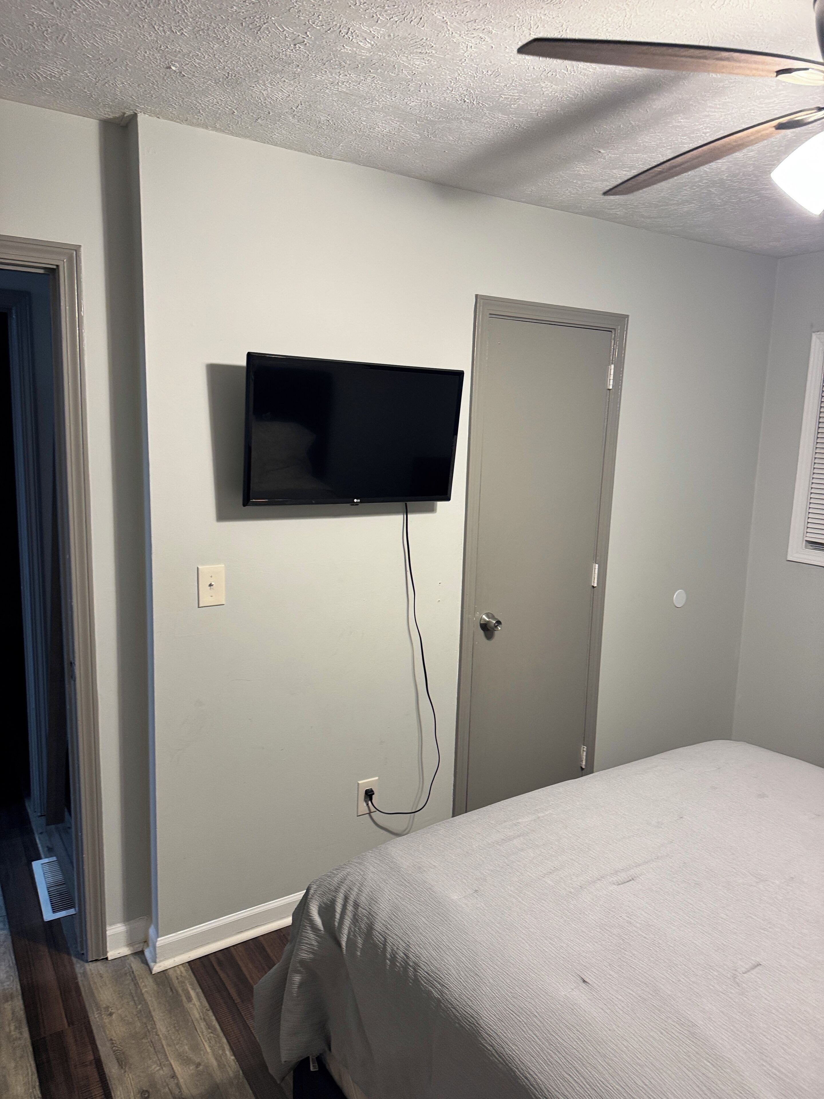 Ein Schlafzimmer mit einem Bett, einem an der Wand befestigten Fernseher, einer Tür und einem Deckenventilator.