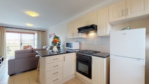A compact kitchen with a stove, microwave, oven, and refrigerator. There is a dining area with a sofa and a table. - Manatoka Coastal Condo (Cape Town)