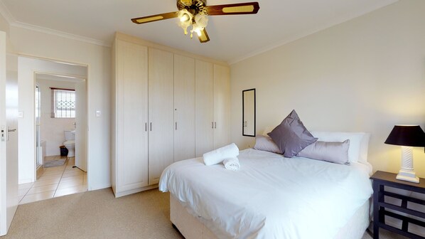 A bedroom with a bed, a nightstand, a ceiling fan, and a wardrobe. - Manatoka Coastal Condo (Cape Town)