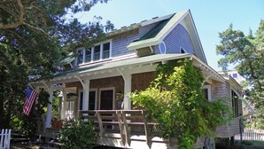 A two-story house with a porch, a small deck, and a flag.