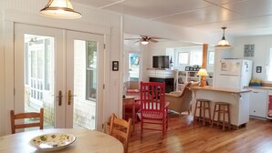 A spacious kitchen with wooden flooring, a dining area with a table and chairs, and a living room with a red chair.