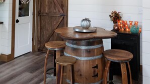 Un interior rústico con una mesa de barril de madera, taburetes, un arreglo decorativo y una puerta corredera de estilo granero.