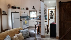 Una sala de estar acogedora con un sofá gris, una mesa de centro de madera y una zona de cocina con armarios blancos, una estufa y un microondas.