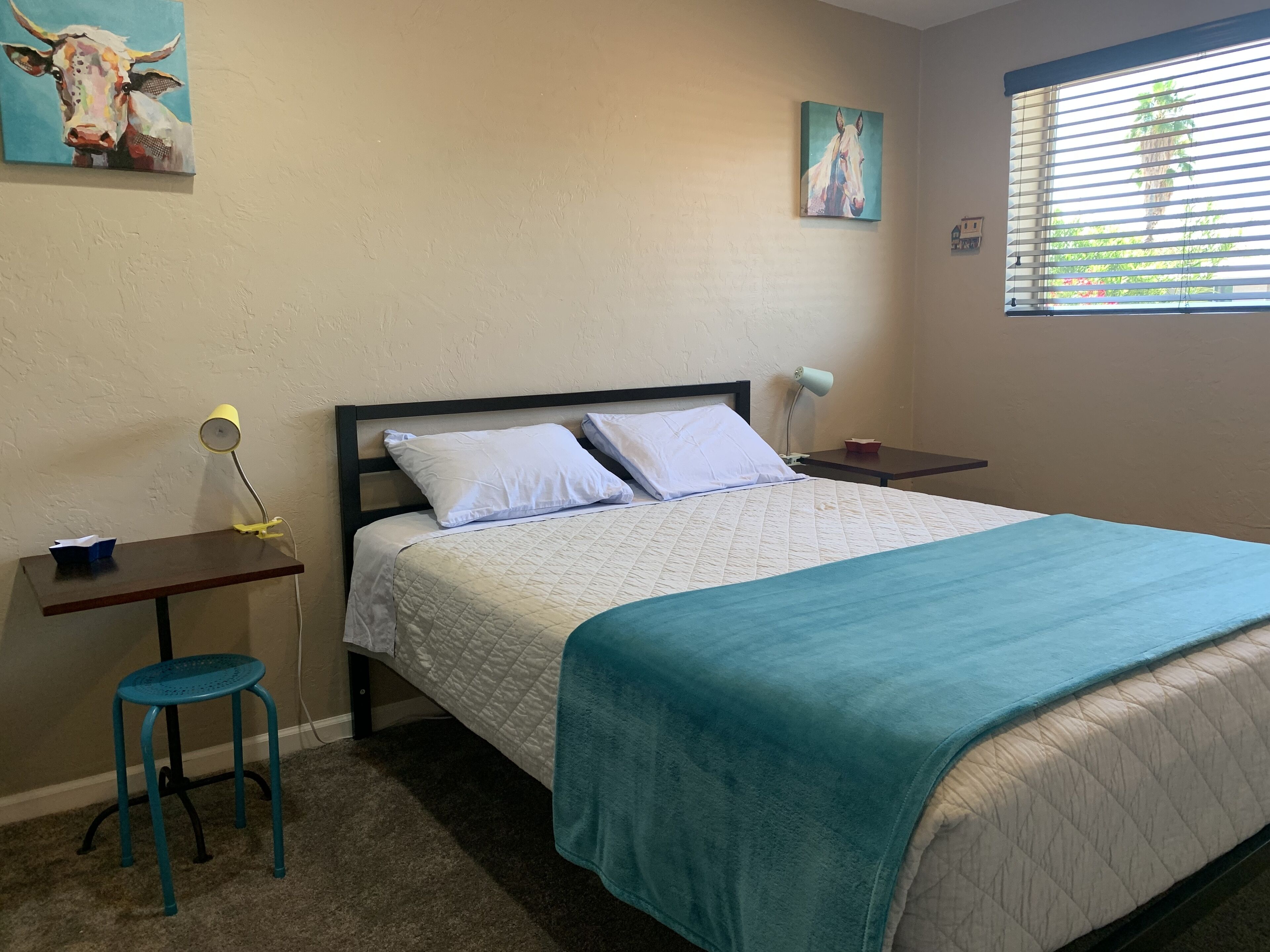 Une chambre bien rangée, avec un lit, un bureau, une chaise et une fenêtre équipée de stores.