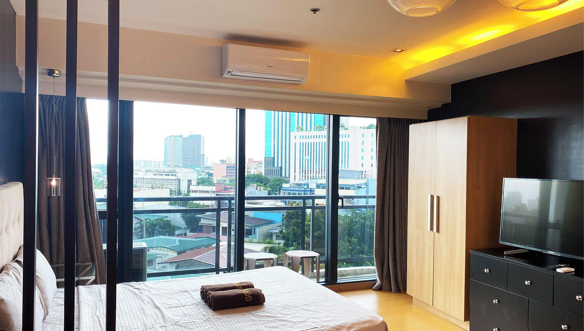 A modern hotel room with a large bed, a TV, a wardrobe, and a balcony with a city view.