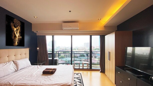 Habitación de hotel moderna con una cama grande, un televisor de pantalla plana y vistas a la ciudad a través de amplias ventanas.