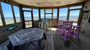 A wooden deck with a table and stools, overlooking a beach and ocean. - Soundview:  Dog friendly sound front home, den, private dock. (Ocracoke)