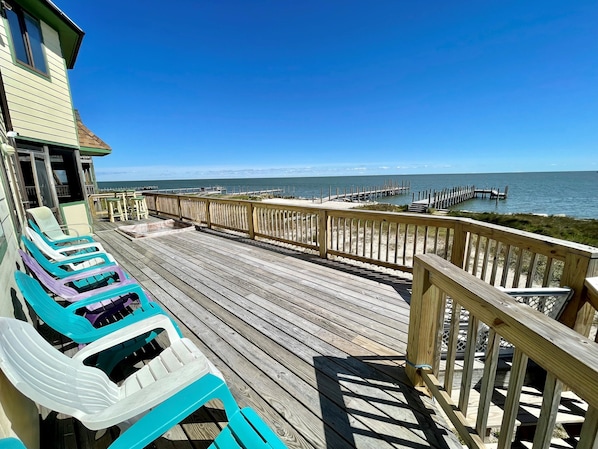 A wooden deck with beach chairs, a view of the ocean, and a pier.