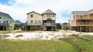 A beachfront property with multiple houses, including a prominent yellow building with a tower and a green building with a balcony. - Soundview:  Dog friendly sound front home, den, private dock. (Ocracoke)