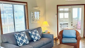 A living room with a grey sofa, a wooden coffee table, a wicker armchair, and a ceiling fan. - Soundview:  Dog friendly sound front home, den, private dock. (Ocracoke)
