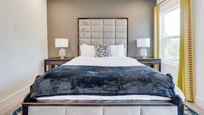 A hotel room with a large bed, two bedside tables with lamps, a headboard, and a window with curtains. - Funky | Whimsical |Steps from Highland Park (Dallas)