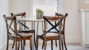 A dining area with a round table and four chairs, a potted plant, and a window with a view of a brick building. - Funky | Whimsical |Steps from Highland Park (Dallas)