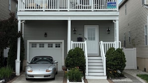 Une maison à deux étages avec un balcon, un garage et une allée où est garée une voiture.