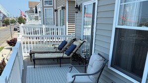 Une véranda avec deux fauteuils et une table, une balustrade blanche et une vue sur la rue.