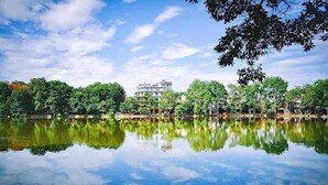 A calm lake with reflections of trees and a building in the background. - Hong Ngoc Hotel (Yen Bai)