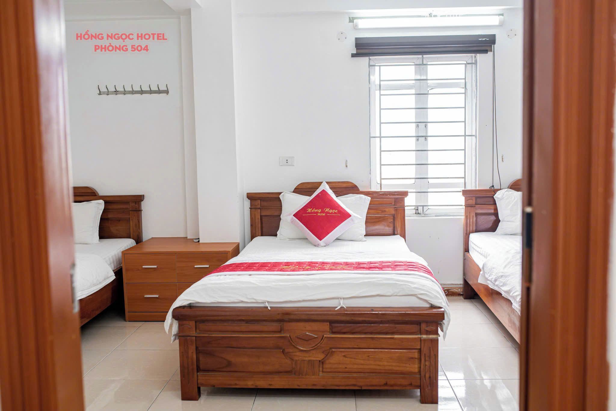 Een hotelkamer met een houten bed, een nachtkastje, een lade, een raam met zonwering en een aan de muur bevestigd telefoon.