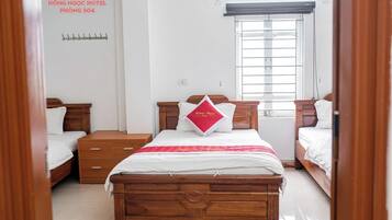 Een hotelkamer met een houten bed, een nachtkastje, een lade, een raam met zonwering en een aan de muur bevestigd telefoon.
