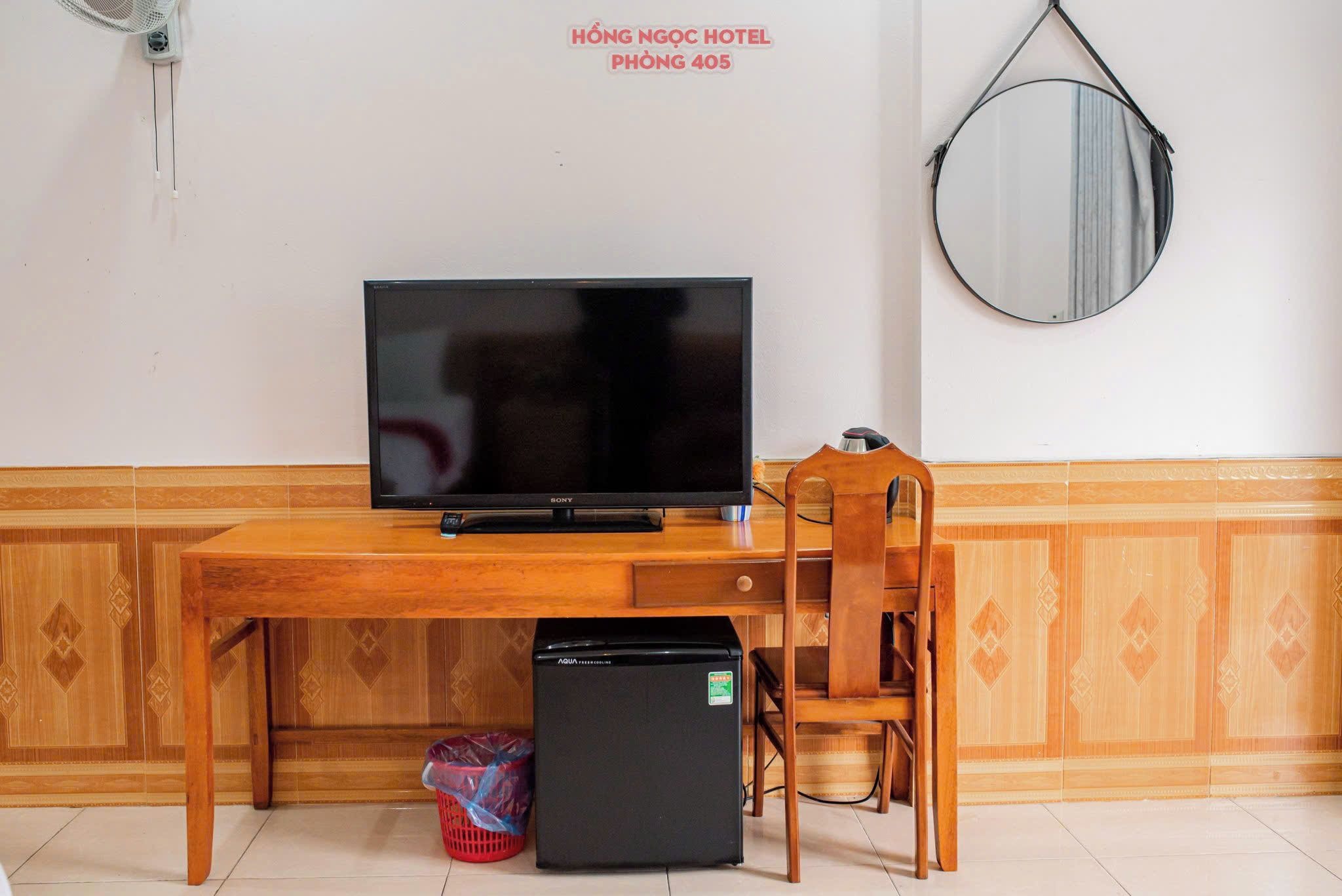 Une pièce comprenant un bureau en bois, une télévision, un réfrigérateur, une chaise et un miroir fixé au mur.