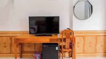Une pièce comprenant un bureau en bois, une télévision, un réfrigérateur, une chaise et un miroir fixé au mur.