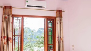 A bedroom with a bed, an air conditioning unit, a window with curtains, and a view of greenery outside. - Hong Ngoc Hotel (Yen Bai)