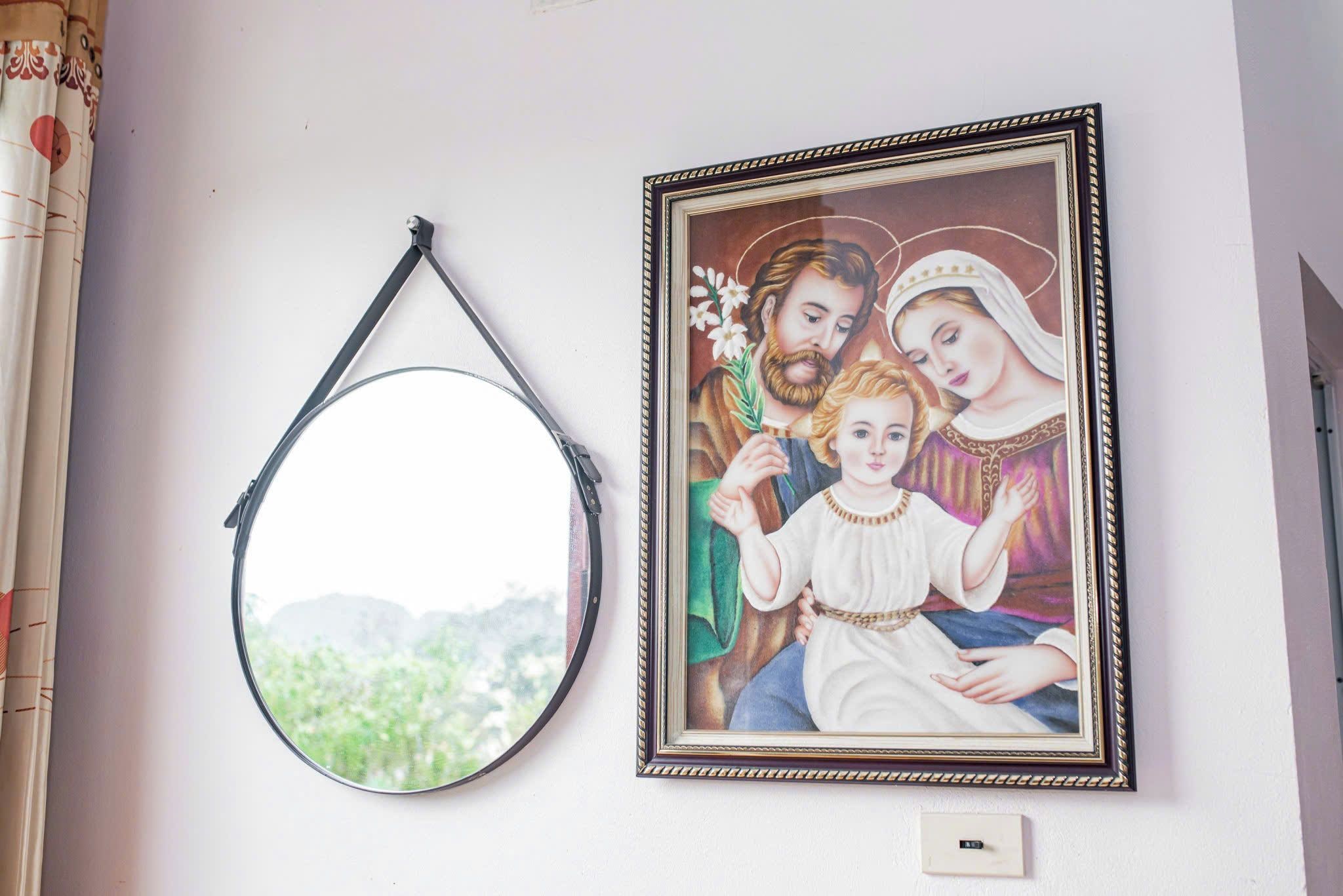 A framed religious painting on a wall, a round mirror, and a small plaque below the painting.
