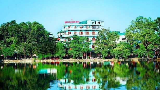 A multi-story hotel with balconies, situated by a lake with reflections of the building and trees. - Hong Ngoc Hotel (Yen Bai)
