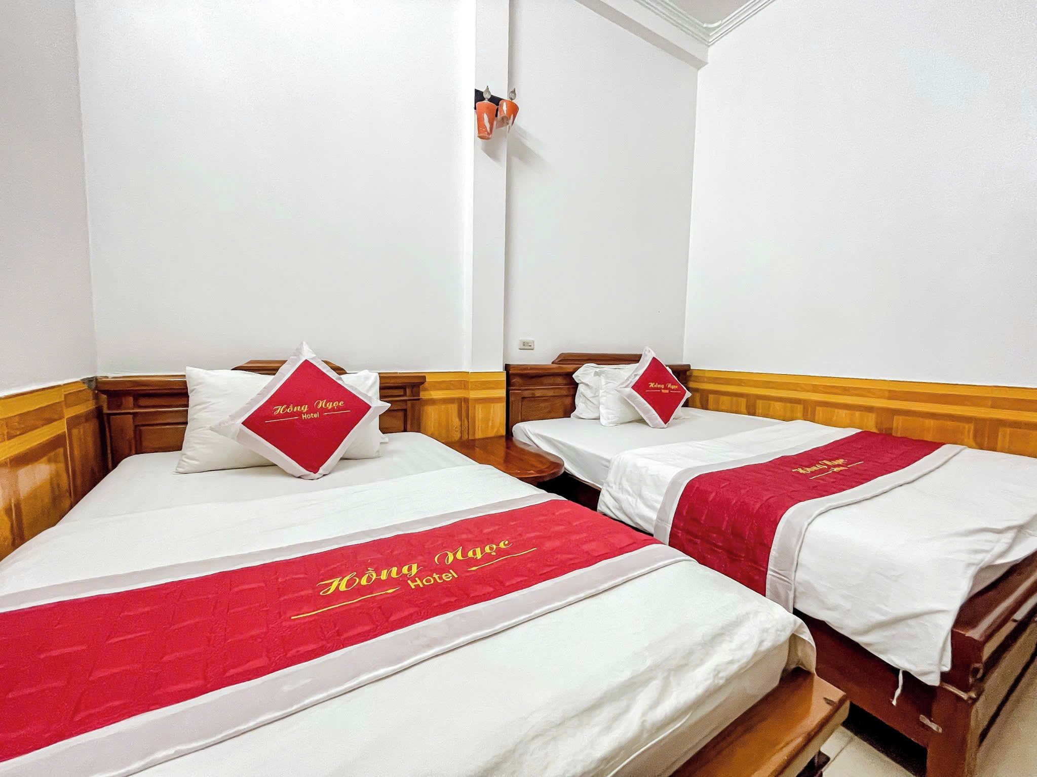 Dos camas individuales con ropa de cama roja y blanca, cabeceros de madera y una pared blanca con un interruptor de luz.