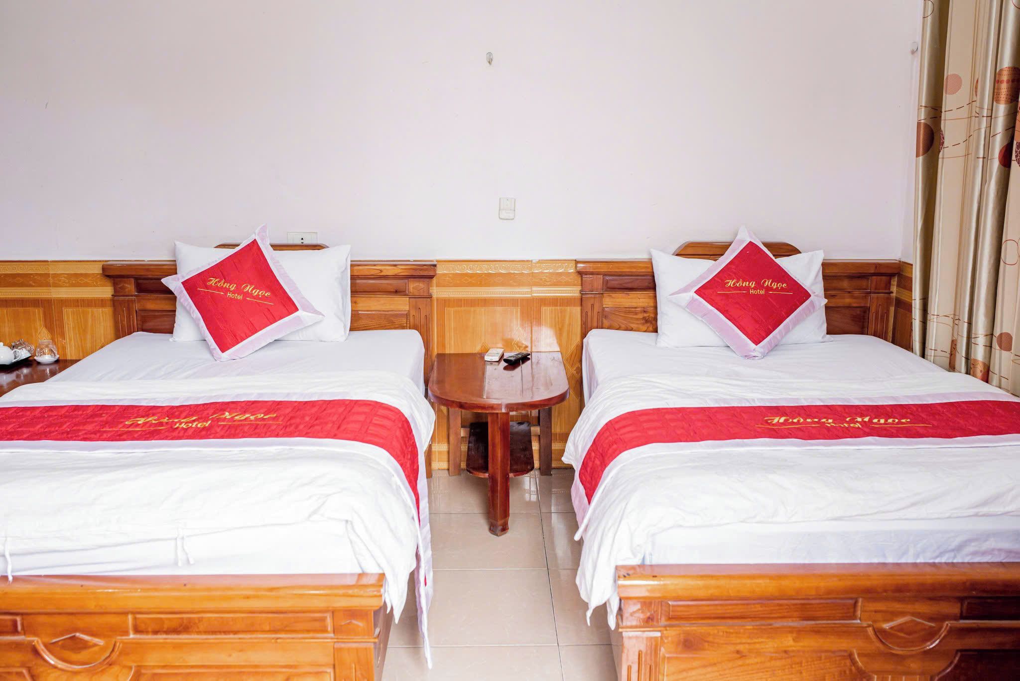 Une chambre d’hôtel avec deux lits, chacun doté d’une tête de lit en bois, d’une petite table en bois et d’une table de chevet avec une lampe.