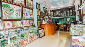 A room with a wooden reception desk, framed artwork on the walls, and glass display cases with various items. - Hong Ngoc Hotel (Yen Bai)