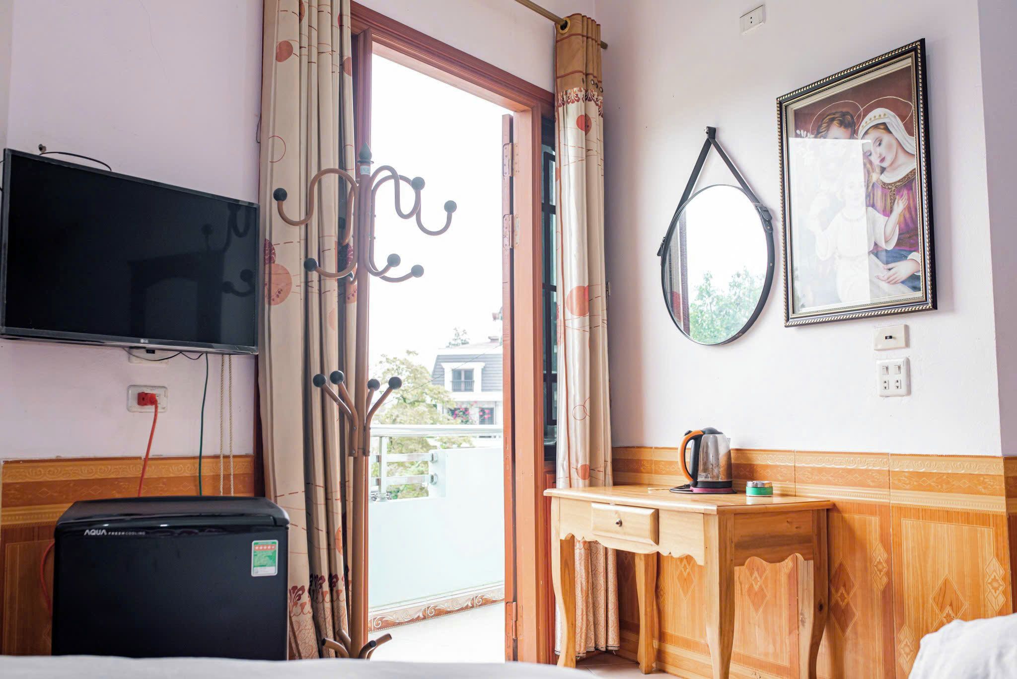 A hotel room with a television, a wooden desk, a kettle, and a framed picture on the wall.