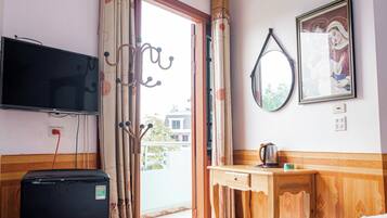 A hotel room with a television, a wooden desk, a kettle, and a framed picture on the wall.
