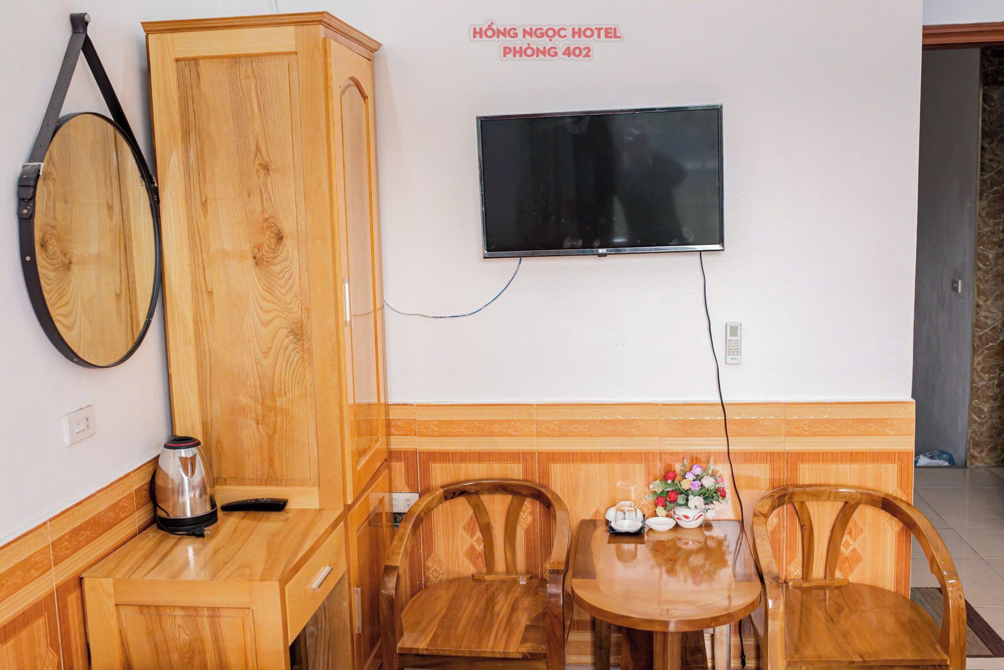 A hotel room with a wooden cabinet, a television mounted on the wall, a table with chairs, and a small table with a vase of flowers.
