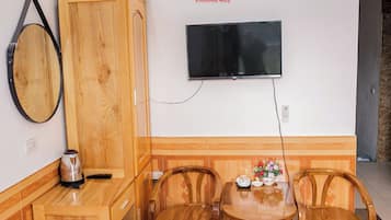 A hotel room with a wooden cabinet, a television mounted on the wall, a table with chairs, and a small table with a vase of flowers.
