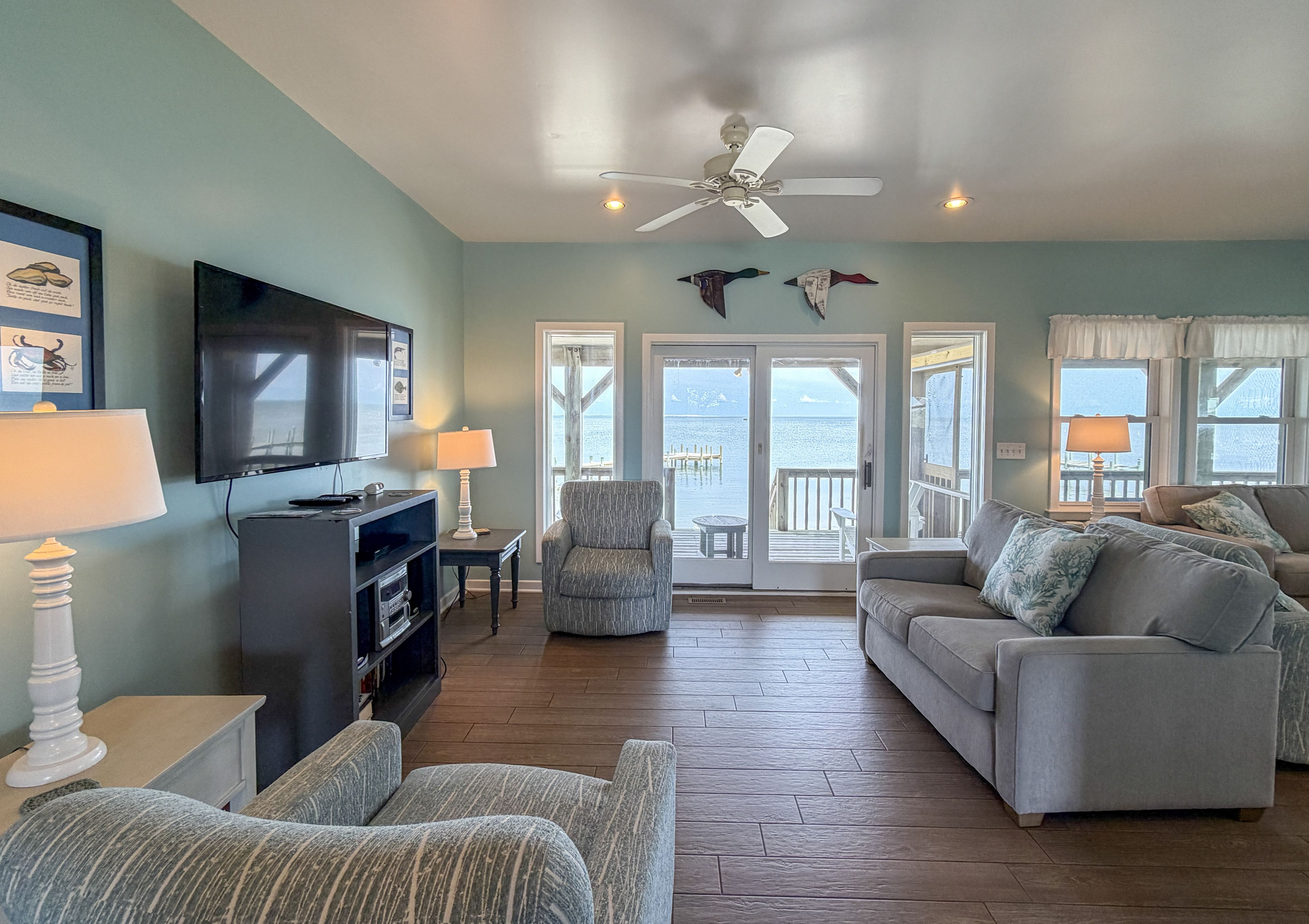 A living room with a television, seating, a ceiling fan, and a view of the outdoors.
