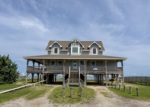 A two-story wooden house with a balcony, a porch, and a staircase leading to the main entrance. - Anticipation:  Private dock, wrap around deck, expansive sound views. (Ocracoke)