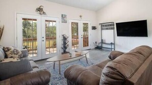 A living room with a brown leather couch, a coffee table, and a TV mounted on the wall. There are sliding glass doors leading to an outdoor area.
