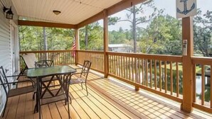 A covered deck with a table and chairs, a ceiling fan, and a view of trees and a flag.
