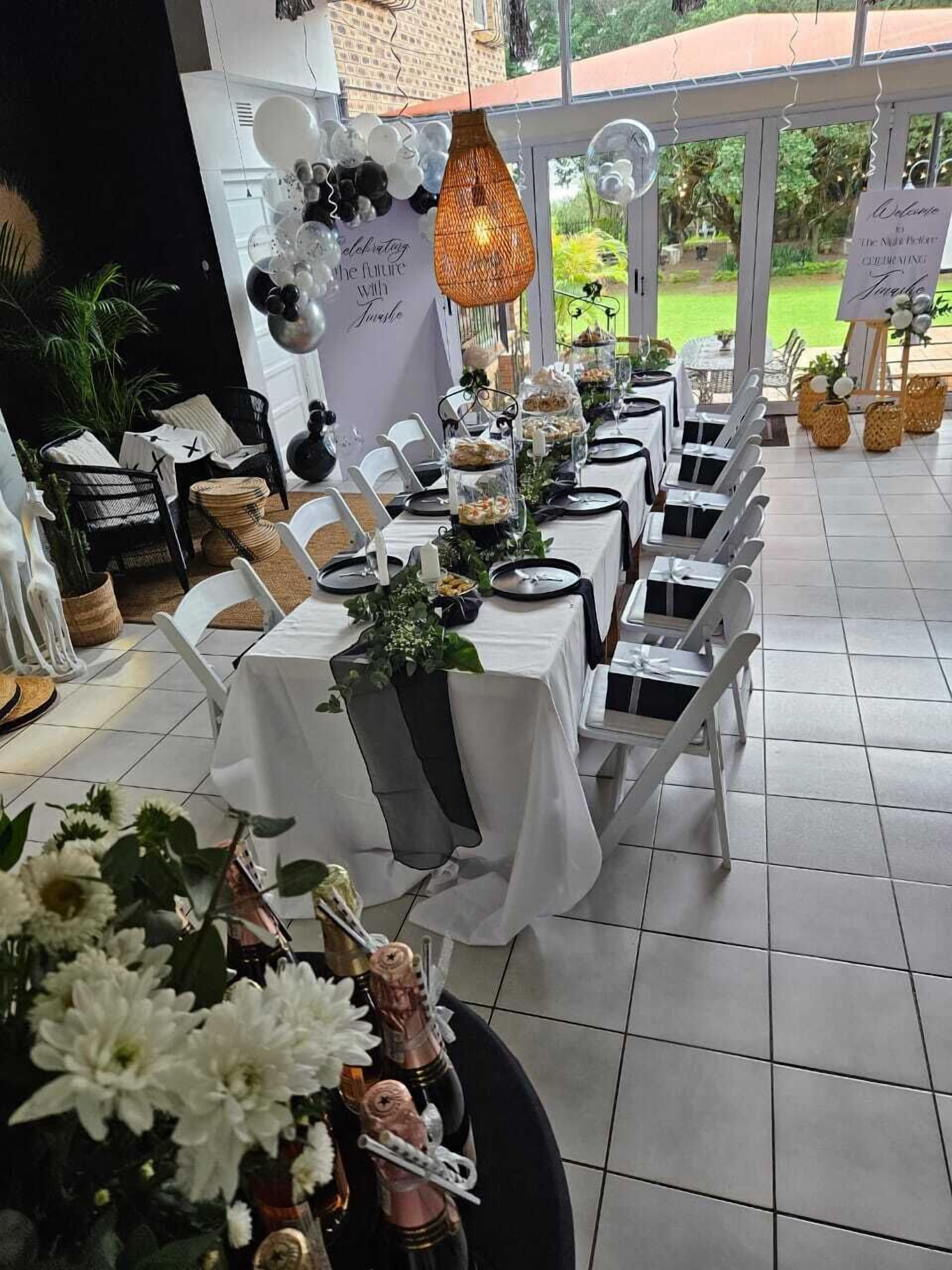 A long table set for a formal event with white tablecloths, black chairs, and a decorative centerpiece.