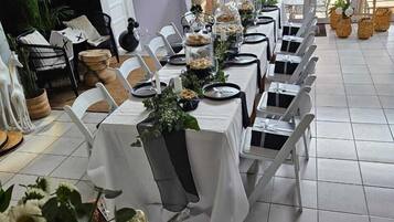 A long table set for a formal event with white tablecloths, black chairs, and a decorative centerpiece.