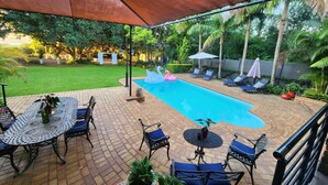 A covered outdoor area with a swimming pool, lounge chairs, and a garden. - Hillton Manor Guest House (Richards Bay)