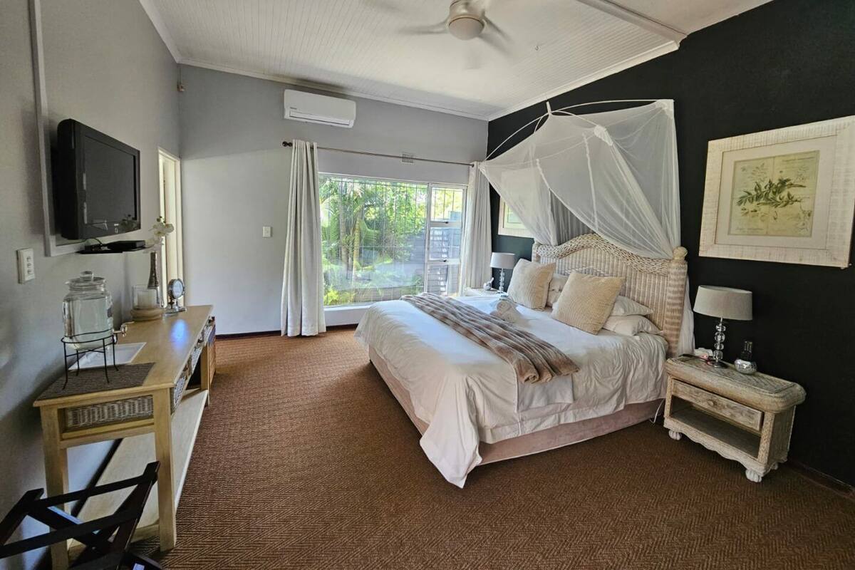 A bedroom with a bed, bedside table, nightstand, TV, and a window with curtains.