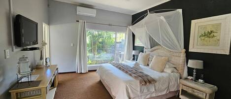 A bedroom with a bed, bedside table, nightstand, TV, and a window with curtains.