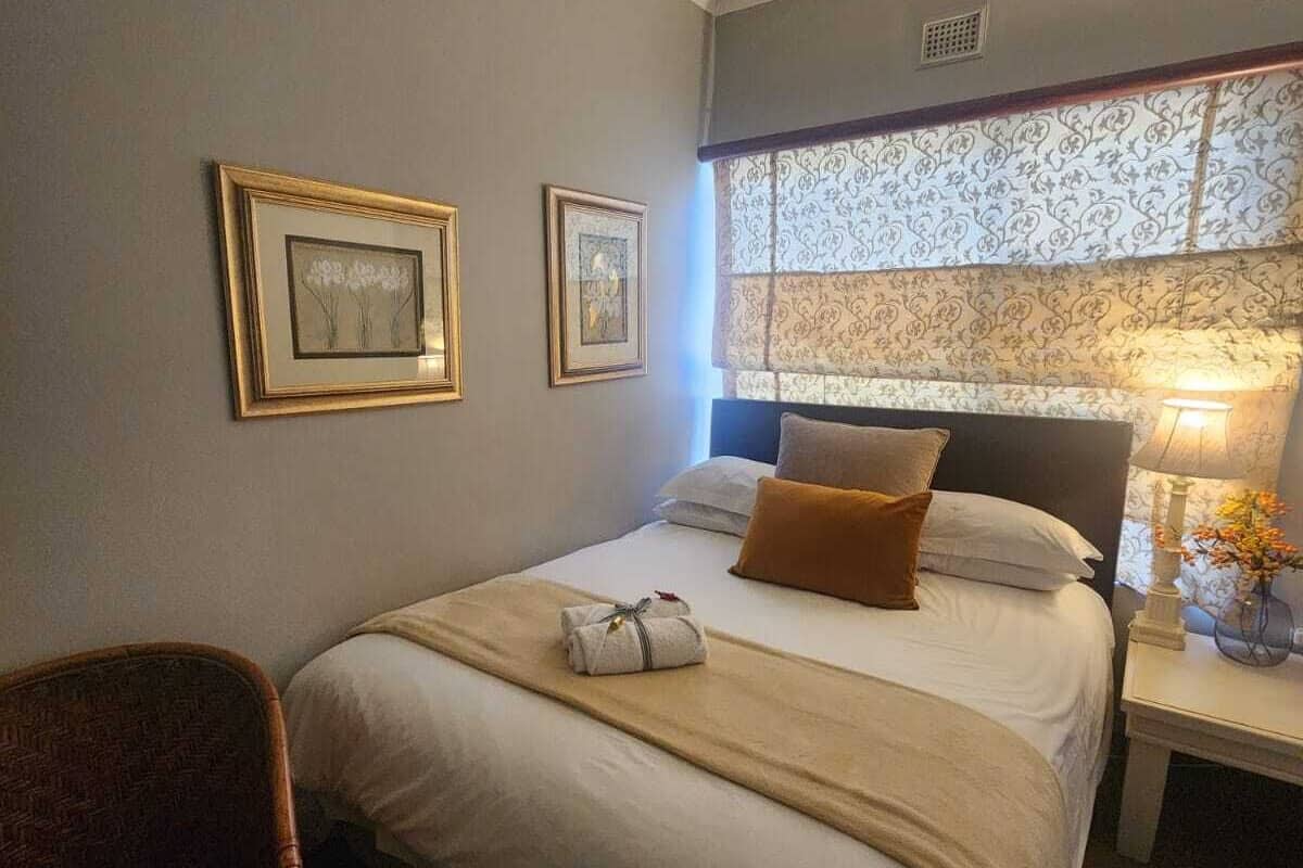 A neatly arranged hotel room with a bed, a chair, and a nightstand with a lamp.