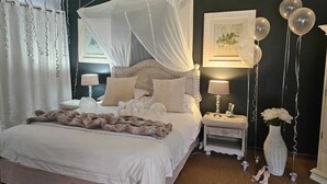 A bedroom with a four-poster canopy bed, bedside tables with lamps, a vase with flowers, and balloons. - Hillton Manor Guest House (Richards Bay)