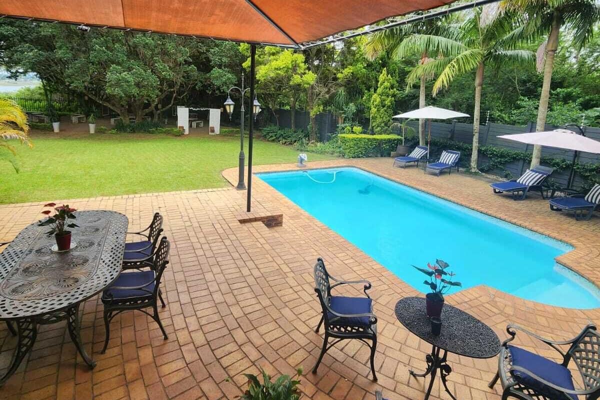 A covered outdoor area with a pool, lounge chairs, and a table with chairs.