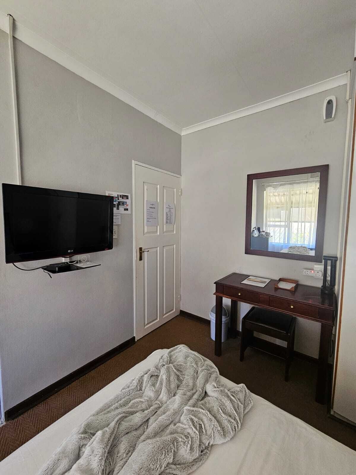 A hotel room with a bed, a desk with a chair, a television mounted on the wall, and a window with curtains.