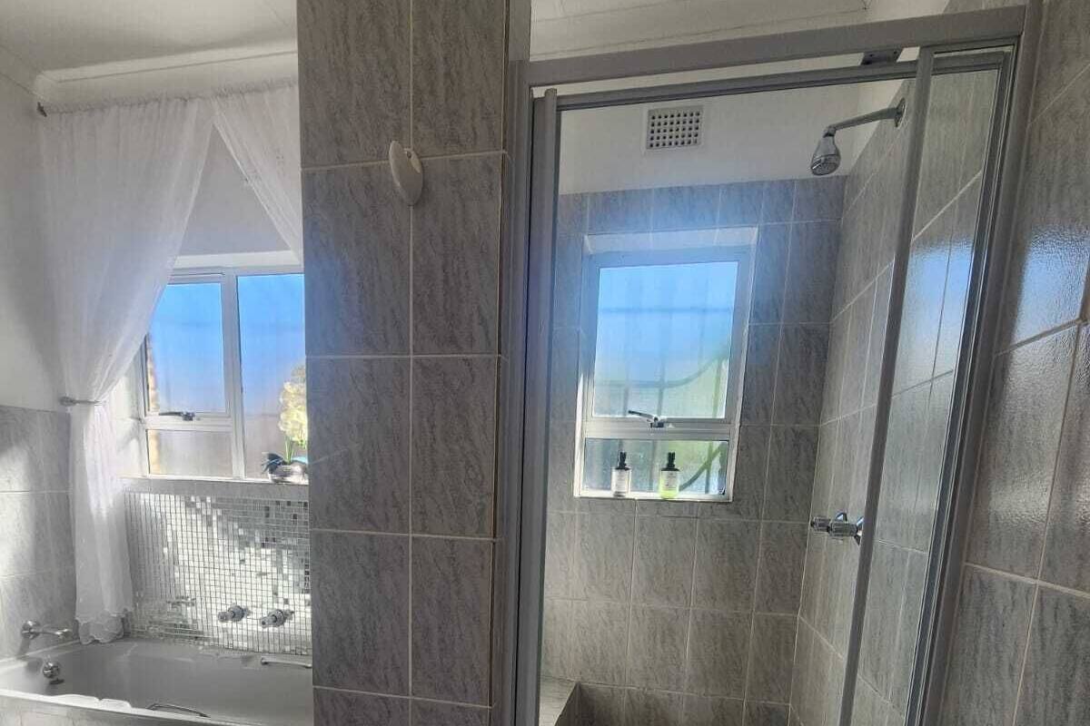 A modern bathroom with a glass-enclosed shower, a bathtub, and a window with a view.